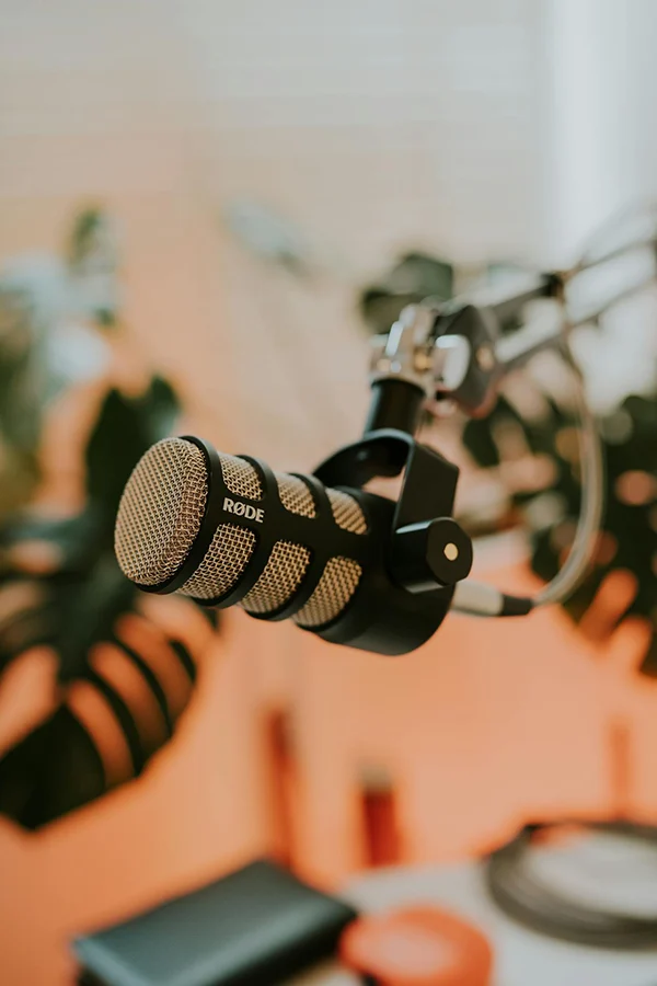 Close-up of a podcast microphone suspended on a boom arm in a softly lit recording studio.